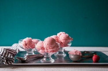 Three glass bowls full of strawberry ice cream and a teal background