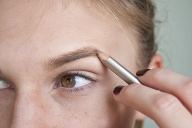 a woman fills in her eyebrows with an eyebrow pencil