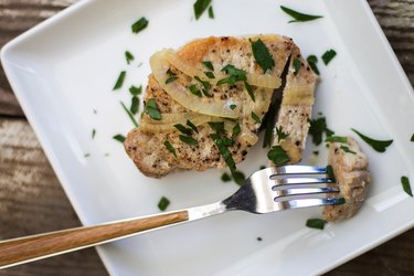 a pork chop and herbs on a white serving plate
