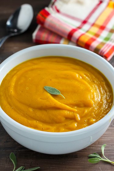 Butternut squash soup in a bowl topped with a sage leaf.