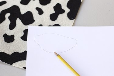 ...A paper and pencil sketch of a cow ear shape over cow print fabric ready to make a cow ear headband