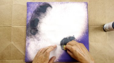 Sponging fabric paint onto cushion cover in circular motion.