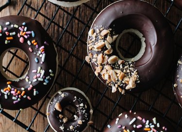Wire rack of chocolate-glazed doughnuts covered with sprinkles and nuts.
