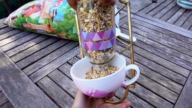 Filling DIY bird feeder made from wrought iron candle sconce and teacup.