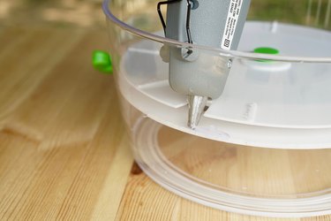 A hot glue gun is shown gluing the the salad spinner top in place