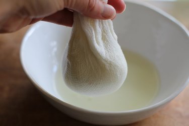 Cheesecloth filled with cauliflower and liquid dripping into a bowl.