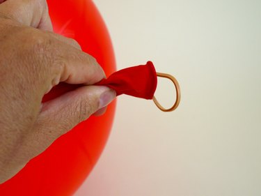 A hand holding the end of the blown balloon with the rubber band sticking out of the mouth.