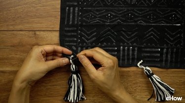 Stitching yarn tassel on DIY mudcloth-inspired wall hanging.