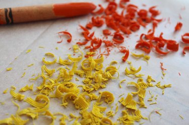 Yellow and orange crayon shavings with an orange crayon on wax paper