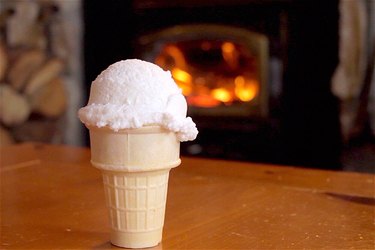 A snow cream cone stands on a table in front of a roaring fire.