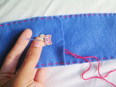 Sewing the owl button onto the felt case.