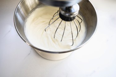 Whipping the cream in a stand mixer until it has formed soft peaks.