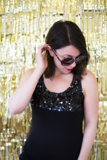 Woman in black dress and glasses posing in front of gold backdrop
