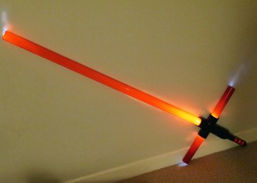 A finished double-blade cross guard light saber lit up against a wall.