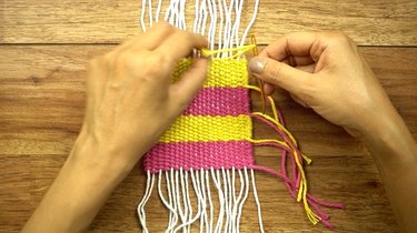 Weaving in loose yarn tails for DIY coasters on a cardboard loom.
