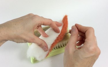 Female hands needle felting orange and white roving on a felting pad