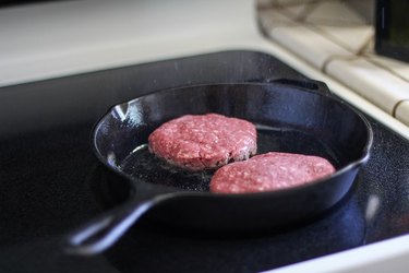 Two burgers cooking in a cast iron skillet