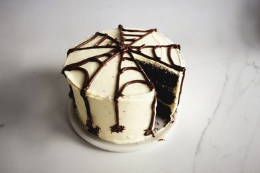 Dark chocolate cake with white frosting and a dark brown spiderweb design
