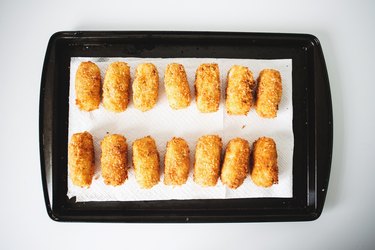 Deep-fried croquettes on a baking tray lined with paper towel.