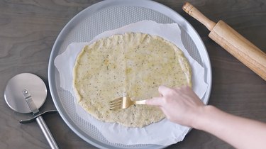 Pricking pizza dough with fork