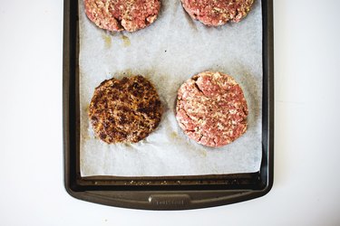 Baking sheet with four burger patties.