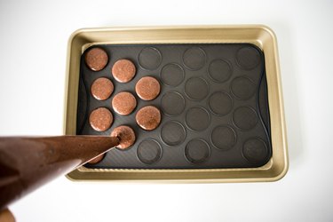 Piping the macarons onto the silicone macaron slip-mat.