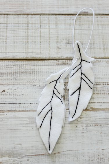 Pair of white felt feathers car air freshener with black embroidered lines of feather center.