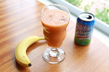 A tropical smoothie with a banana and can of coconut juice on either side.