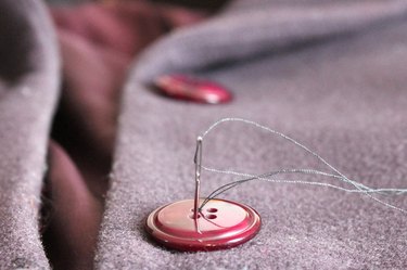 Hand sew a button on the wool coat.