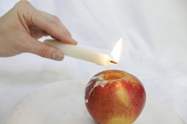 Dripping taper candle wax over apple.
