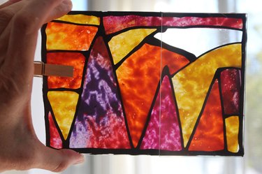 A hand holding up a nearly complete wax paper and melted crayon stained glass window