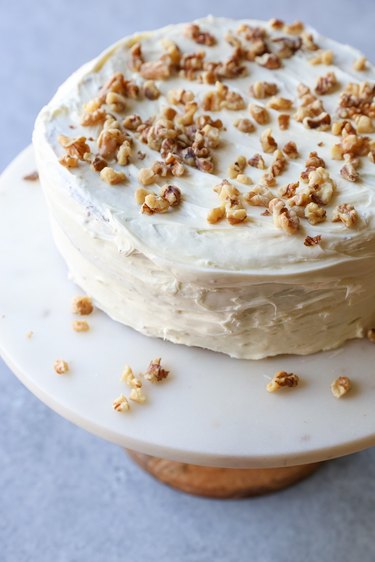Carrot cake on a cake stand with cream cheese frosting and chopped walnuts