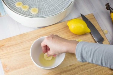 Hand dipping raw banana slices in a bowl of lemon juice.