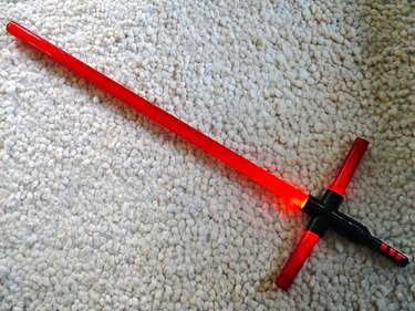 A lit up double-blade cross guard lightsaber against a white background.