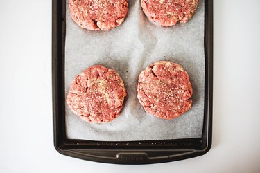 Four hamburger patties on a baking tray.