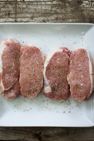 four pork chops with seasoning on them on a white plate