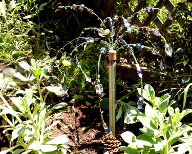 DIY glass beaded garden sparkler in soil among plants.