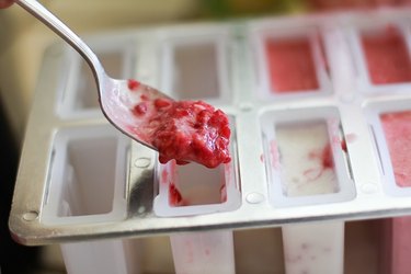 Spoonful of raspberry mixture being added to an ice pop mold.