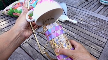 Filling DIY bird feeder made from wrought iron candle sconce and teacup.