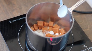 Adding cream to caramel candies in saucepan.