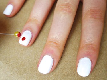 A dot of red polish on a white nail.