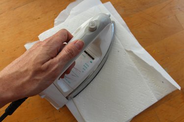 A hand holding and pressing down an electrical iron on top of folded paper towels