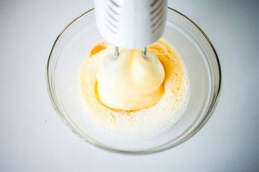 Electric beaters mixing eggs and sugar in a glass bowl.
