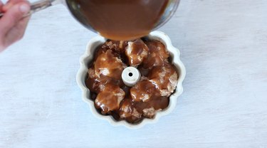 Pouring caramel sauce over rolls in prepared pan.