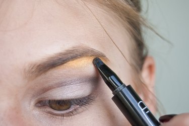 a woman lining her eyebrows with yellow