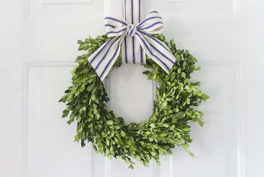 Boxwood wreath hung with blue striped ribbon