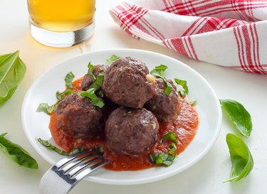 A plate of mozzarella-stuffed meatballs in sauce, topped with fresh basil.