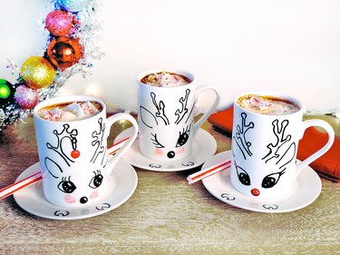 Three white mugs with hand drawn reindeer faces, full of hot chocolate.