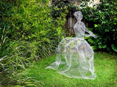 A life sized chicken wire ghost appears barely there in a garden.