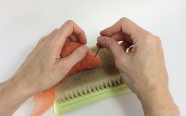 Female hands needle felting orange roving on a felting pad